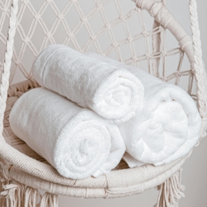 Three rolled white towels elegantly displayed on a stylish macrame chair.